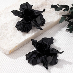 Detailansicht großer schwarzer 3D Blumen-Ohrstecker auf Marmor mit grünen Blättern