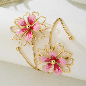 Close-up of golden open arm cuff with two pink enamel cherry blossom flowers