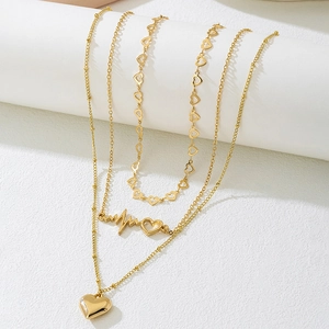 Detailed view of triple-layered golden necklace set featuring heart pendants on a white stand