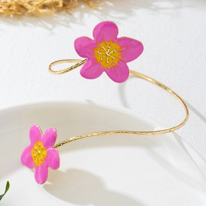 Detail van verstelbare gouden armring met roze emaille bloemen op een wit oppervlak