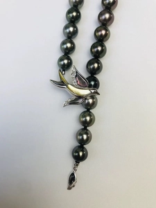 Dettaglio macro del ciondolo rondine con perla nera e madreperla sulla collana elegante