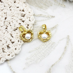 Detail of two heart-shaped gold pendants with white pearls on white lace background