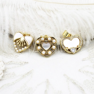 Macro detail of gold heart pendants with pearl and shell inlay on white lace background