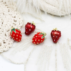 Detailed macro shot of red enamel strawberry charms with gold plating on lace fabric