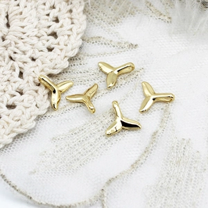 Detailed macro view of five 18K gold plated whale tail charms with polished mirror finish