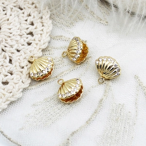 Macro detail of 18K gold plated shell charms with sparkling zircons on white lace background