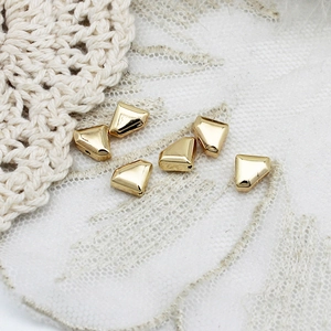 Macro detail of 18k gold plated geometric cross beads on delicate white lace and crochet fabric