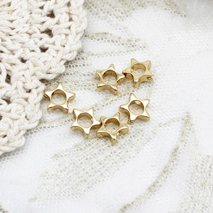 Close-up of six gold star-shaped hollow beads for DIY jewelry making on lace fabric