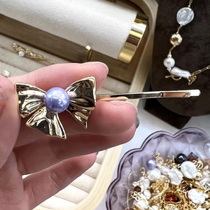 Détail d'une barrette nœud plaquée or 18 carats avec une perle violette centrale élégante