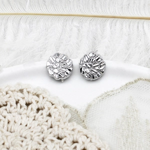 Detailed view of silver stud earrings with unique crushed metal texture on a white tray