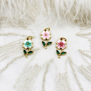 Detailed close-up of enamel flower charms in teal, pink, and red with golden plating