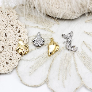 Macro view of ocean jewelry charms featuring pavé jellyfish and conch shells on lace