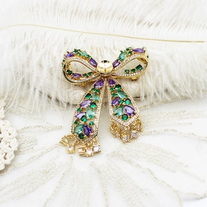 Detail of a luxury gold bow brooch with emerald and purple stones on lace