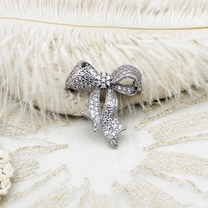 Detail of elegant bow brooch with shimmering zircons on white feather and lace texture