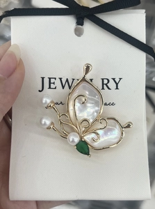 Close-up of golden butterfly brooch with iridescent shell wings and green gemstone