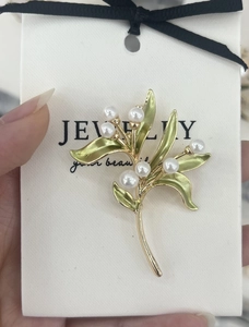 Detailed close-up of a lily of the valley brooch with green enamel leaves and pearls