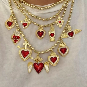 Close-up of layered gold ball chains with red sacred heart pendants and zircon inlay