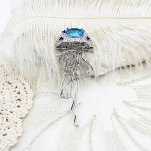 Broche méduse élégante avec pierre bleue et pompons argentés sur dentelle blanche