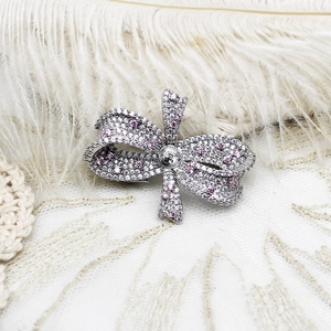 Macro shot of a silver bow brooch with pavé-set pink and white cubic zirconia stones