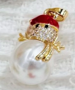 Macro detail of snowman pendant with red enamel hat, white pearl body, and cubic zirconia