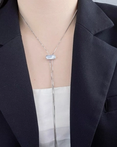Collier en Y argenté avec pendentif bleu porté sur un blazer de style professionnel