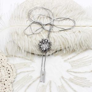 Détail du collier long argenté avec pendentif fleur en zircon et breloques en métal