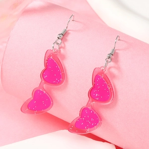 Dettaglio di orecchini a forma di occhiali da sole a cuore rosa glitterati in acrilico