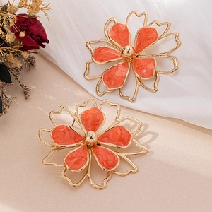 Detail of gold flower earrings with orange marble enamel petals and hollow metal frame