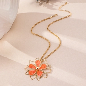 Close-up of golden necklace with orange flower pendant and rope chain detailing