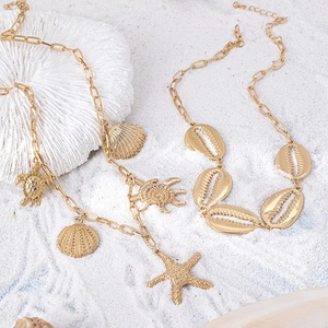 Collana a strati dorata con ciondoli a stella marina e conchiglie su sabbia corallina bianca