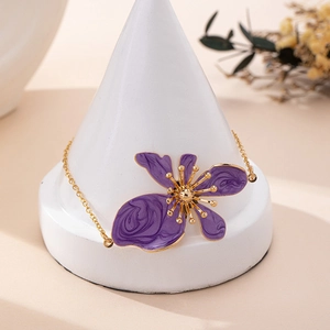 Dettaglio di cavigliera dorata con ciondolo floreale in smalto viola su supporto bianco