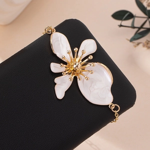 Dettaglio di una cavigliera dorata con un grande fiore in smalto bianco elegante