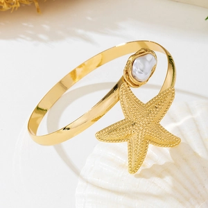 Detail of golden starfish cuff with a baroque pearl resting on a white seashell