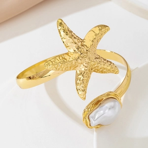 Macro detail of golden starfish and baroque pearl on a textured metal open arm cuff