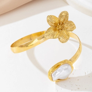 Macro shot of golden floral cuff bracelet featuring a textured flower and white baroque pearl
