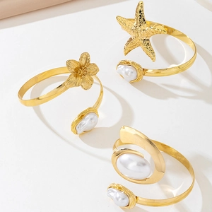 Detail of three gold adjustable arm cuffs with starfish, flower motifs and baroque pearls
