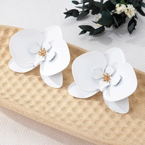 Detail view of 3D matte white orchid earrings with golden stamens on a textured tray