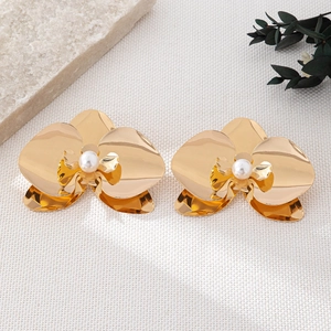 Close-up of golden orchid flower earrings with pearl centers on white fabric background
