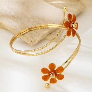 Dettaglio macro di un bracciale a spirale dorato con decorazioni floreali in smalto arancione