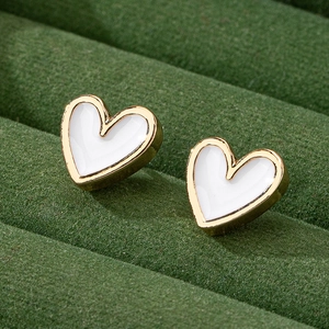 Minimalist heart-shaped gold studs with white enamel on green velvet tray
