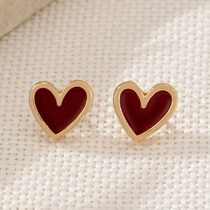 Elegant gold heart earrings with deep red enamel inlay on a textured fabric background