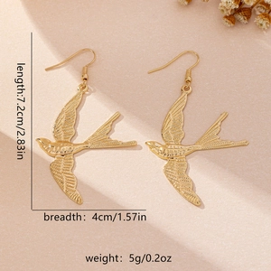 Golden swallow bird drop earrings in minimalist flying pose on textured beige background
