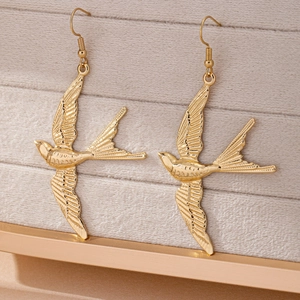 Golden swallow bird drop earrings with engraved feather details on jewelry display