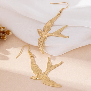 Golden swallow bird drop earrings with textured wing details on soft silk background