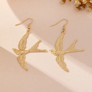 Macro shot of gold-plated swallow drop earrings showing intricate wing feather textures