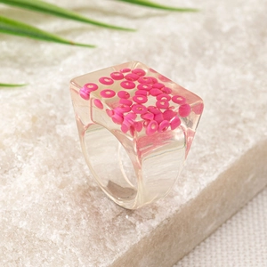 Macro view of transparent resin ring featuring embedded vibrant pink round beads