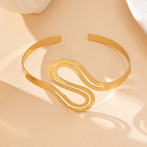 Detailopname van een gouden metalen open armband met een artistiek S-vormig golfontwerp