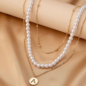 Elegant multi-layered gold pearl necklace featuring a round letter A initial pendant