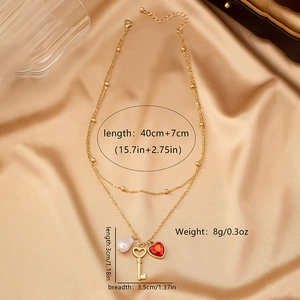 Detalle de colgante de llave de corazón, perla y gema roja en collar dorado de capas