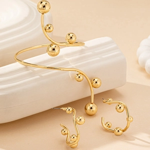 Set orecchini a C e bracciale rigido dorato con sfere metalliche su espositore moderno
